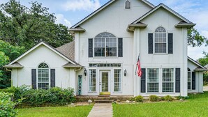 Een woonhuis met twee verdiepingen, een veranda, een bord met de tekst 'welkom' en een Amerikaanse vlag.