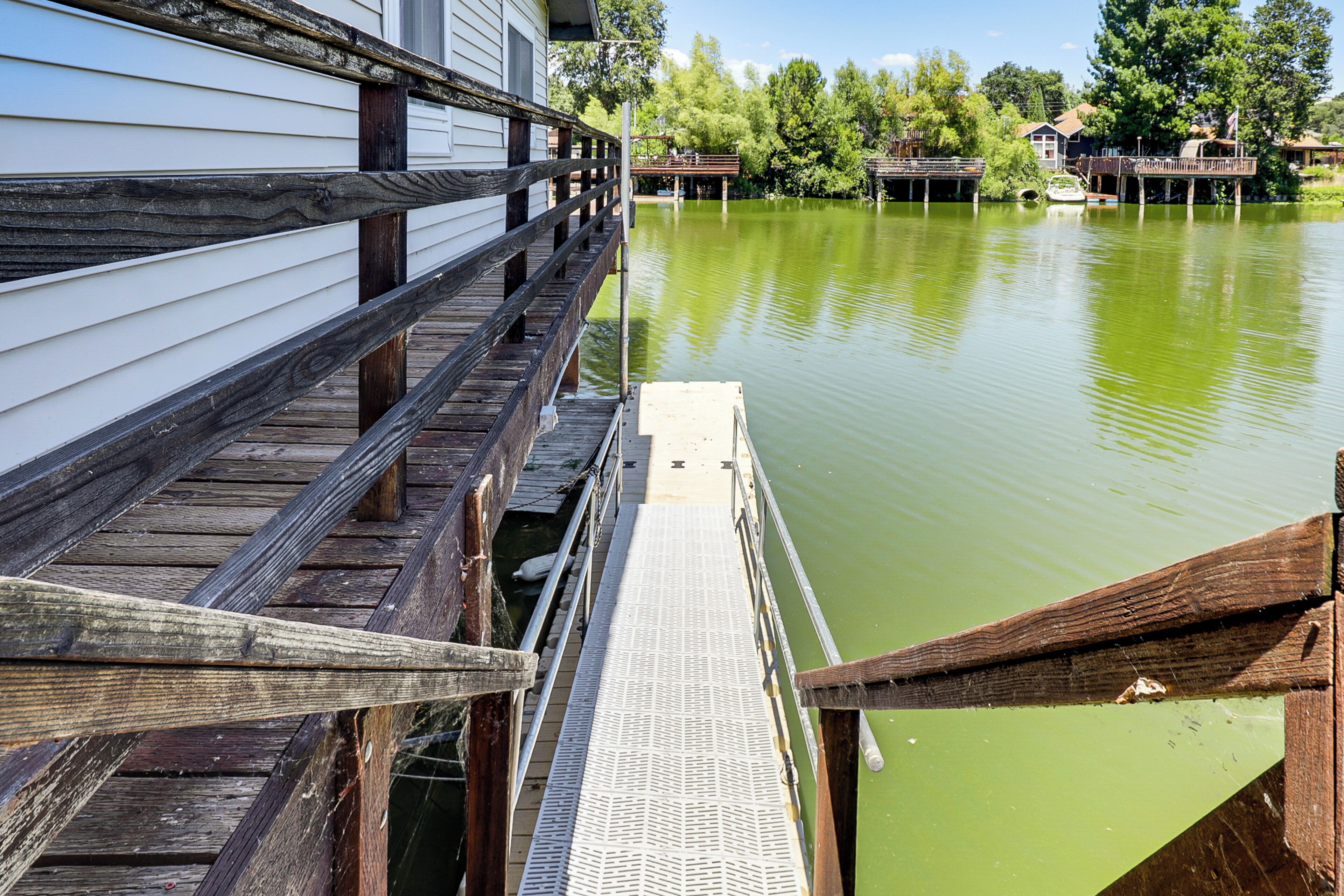 Un muelle de madera que se extiende sobre un lago tranquilo, con una casa a la izquierda y un bote en el agua.