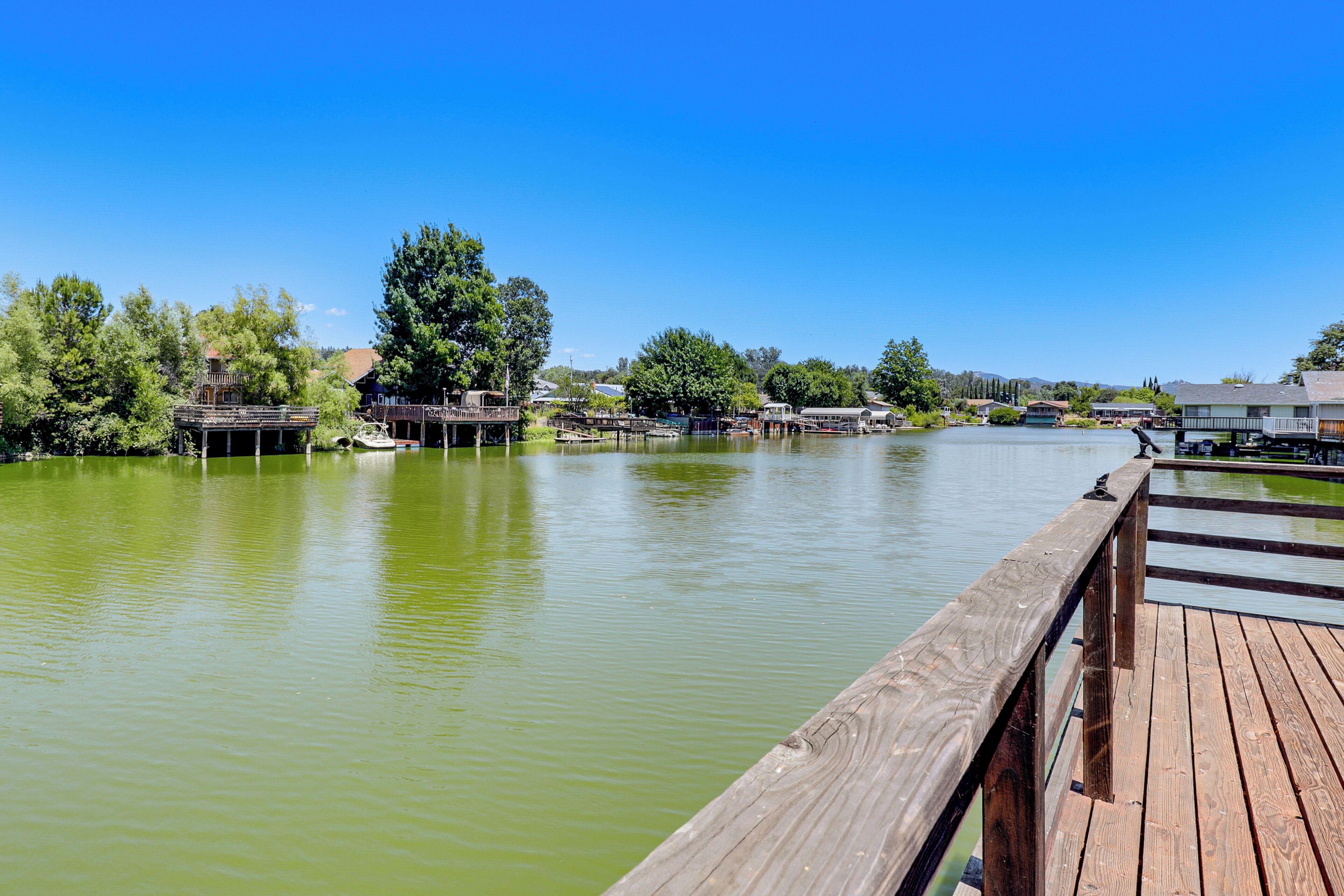 A wooden dock extending into a calm lake with buildings and trees in the background.
