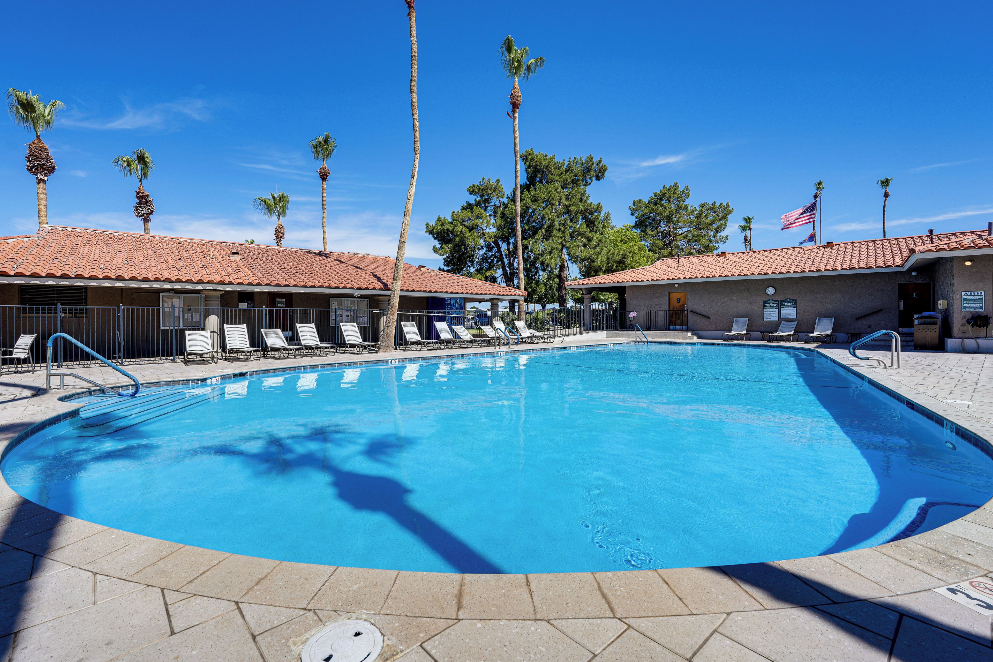 A swimming pool with lounge chairs, palm trees, and a building with a tiled roof.