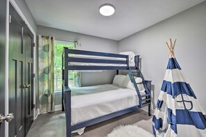 Ein Stockbett mit weißer Matratze und blauem Gestell, ein flauschiger, weißer Teppich, ein blau-weiß gestreiftes Zelt und ein Fenster mit Vorhängen.
