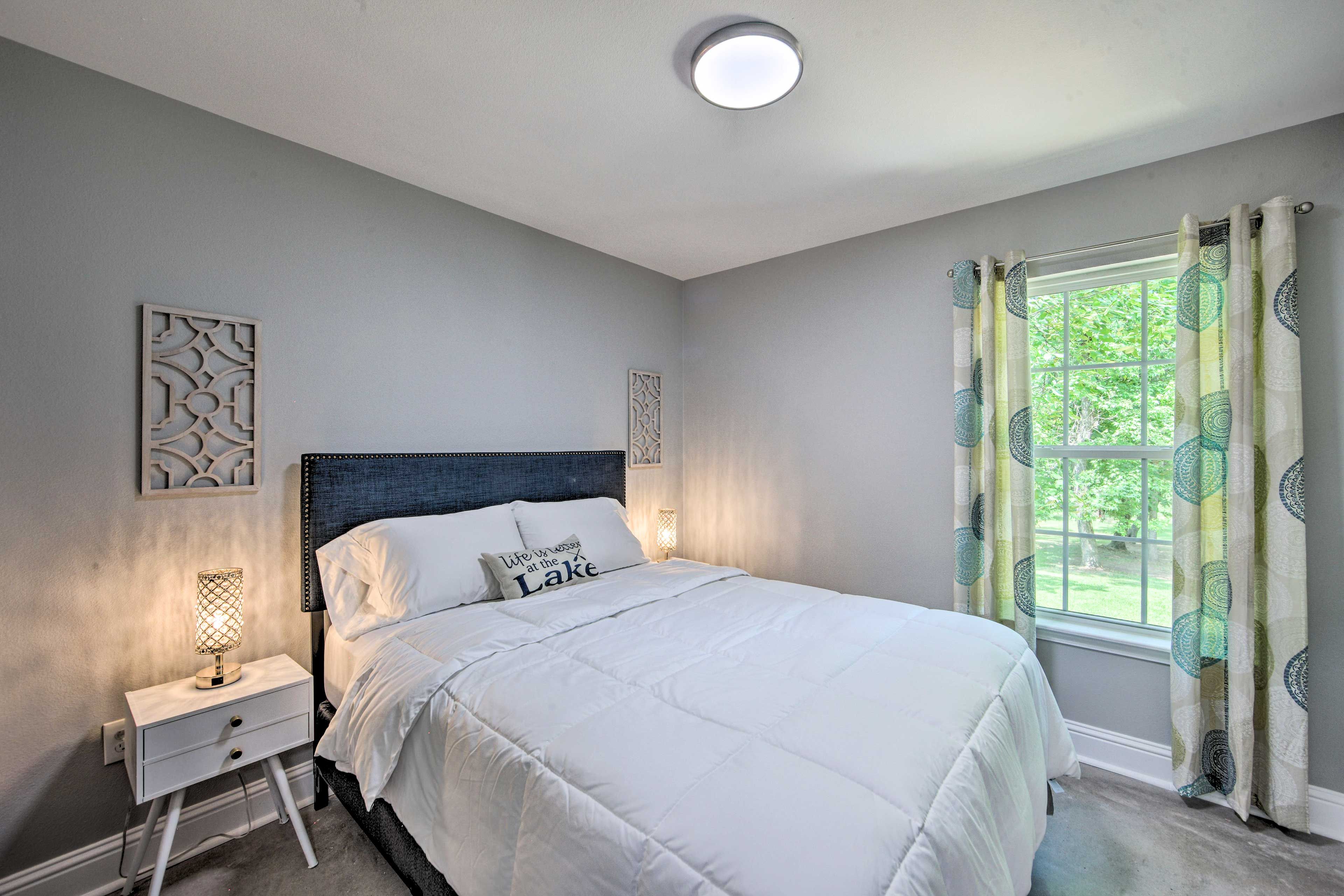 A bedroom with a bed, nightstand, and window with curtains.