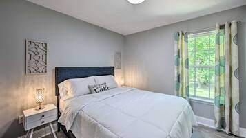 A bedroom with a bed, nightstand, and window with curtains.