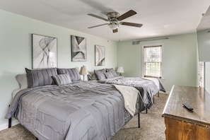 A bedroom with two beds, a ceiling fan, artwork on the walls, a window with blinds, and a wooden table. - Timeless Charm in the Heart of Steubenville (Steubenville)