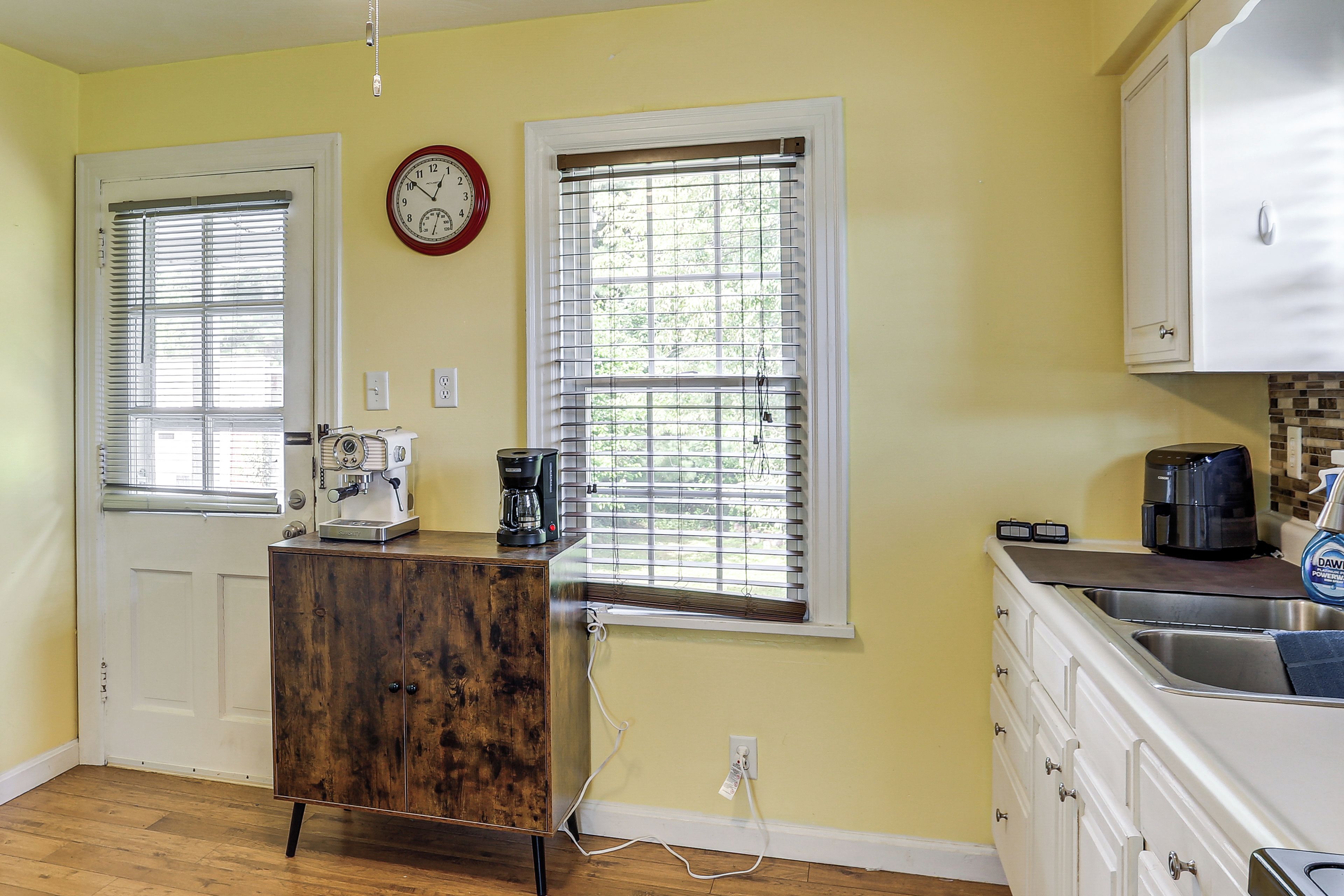 A kitchen with a coffee maker, a clock, and a window with blinds.