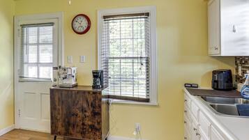 A kitchen with a coffee maker, a clock, and a window with blinds.