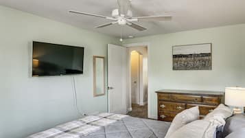 A bedroom with a bed, a ceiling fan, a dresser, a television, and a door leading to another room.