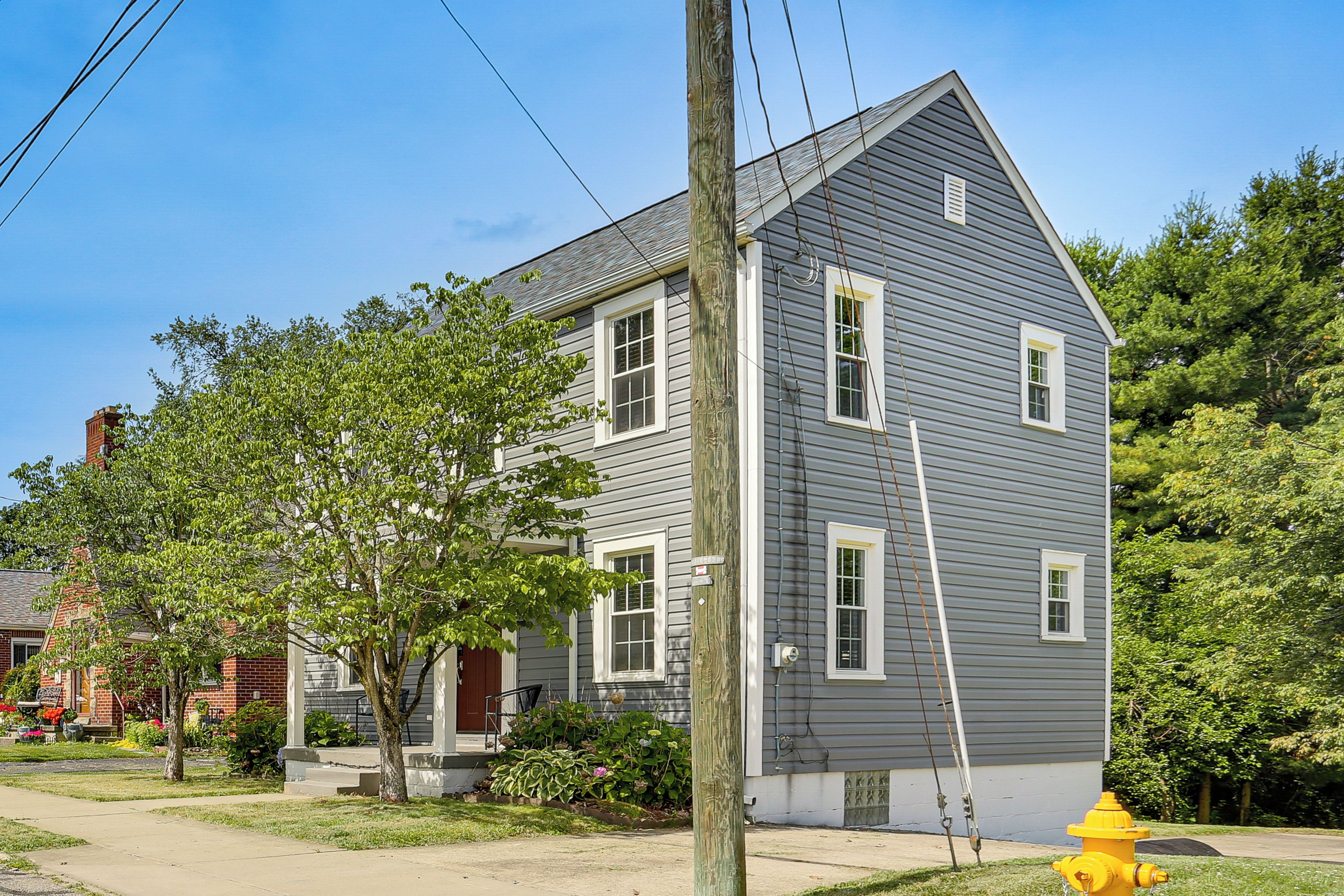 A two-story house with a gray exterior, white trim, and a yellow fire hydrant in front.