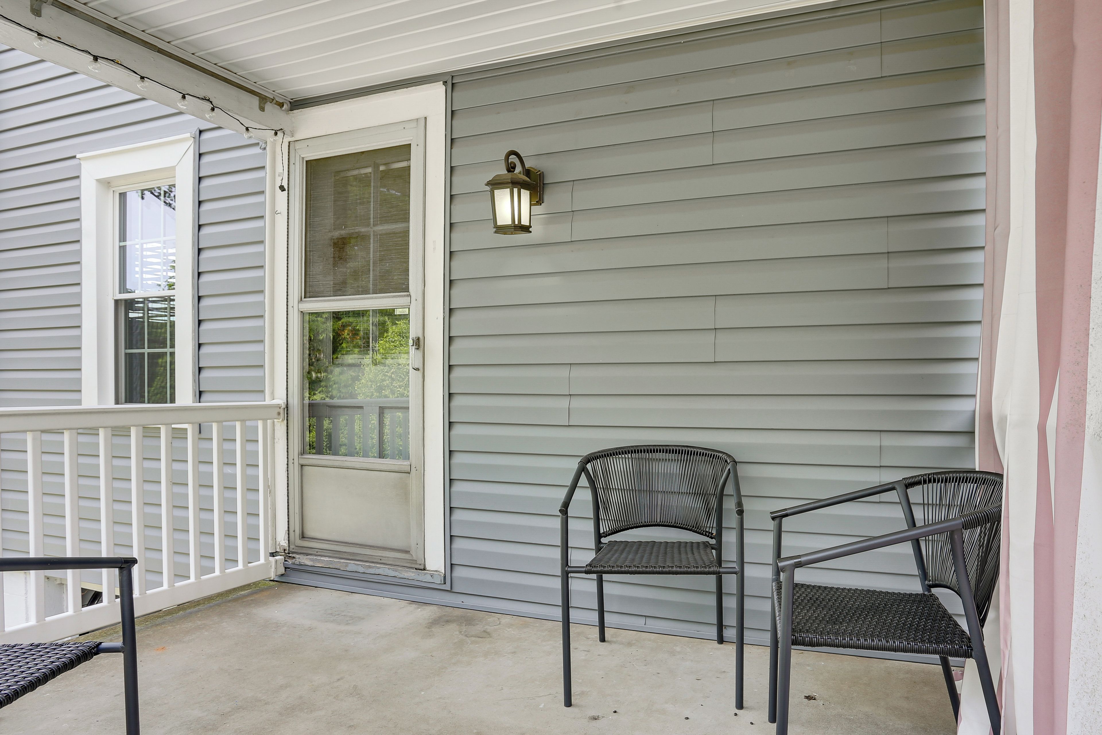 A porch with a white door, a black metal chair, and a wall-mounted lantern.