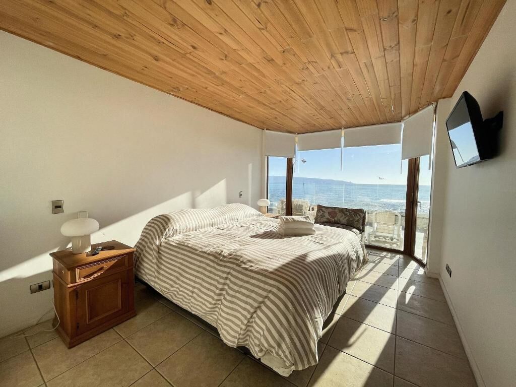 A bedroom with a bed, wooden nightstand, and a view of the sea.