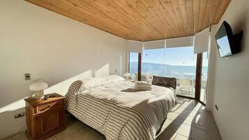 A bedroom with a bed, wooden nightstand, and a view of the sea.