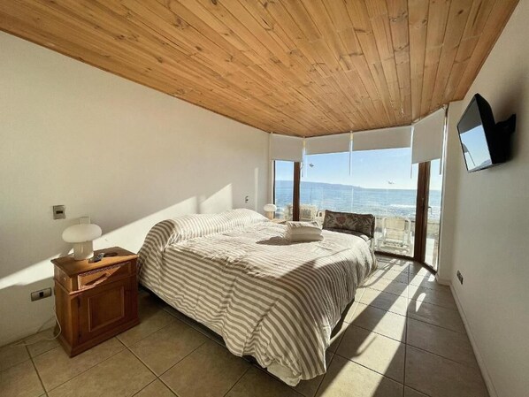 A bedroom with a bed, wooden nightstand, and a view of the sea. - Rbk Único y amplio depto. frente al mar (Concón)