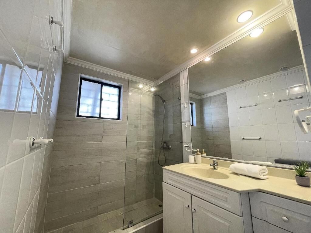 Un baño con cabina de ducha de vidrio, un lavabo con espejo y una ventana.
