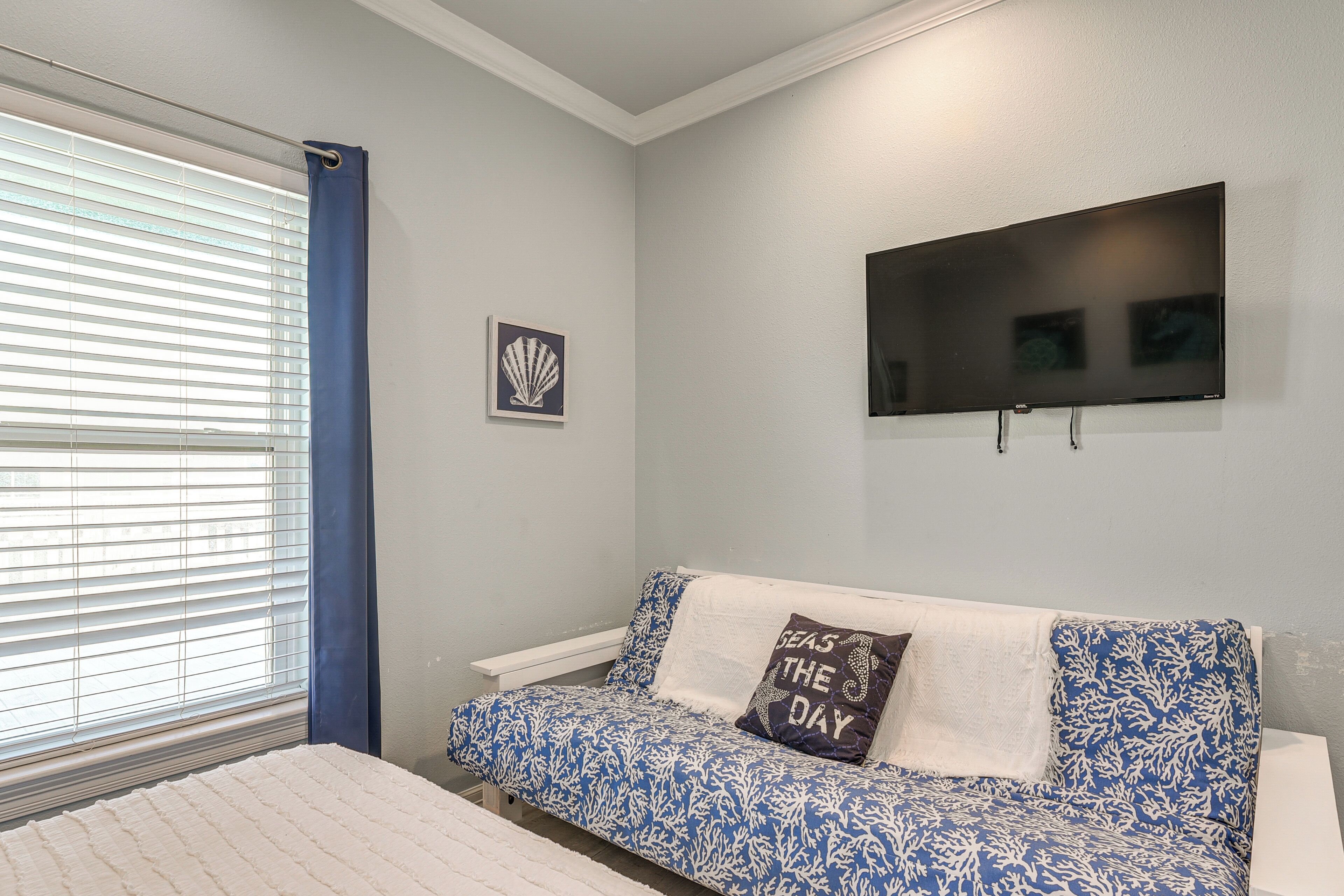 A room with a bed, a blue patterned sofa, a television, and a window with blinds.