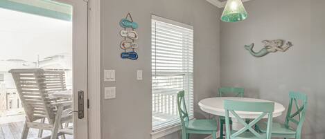 A dining area with a round table and chairs, a window with blinds, and a hanging light fixture.