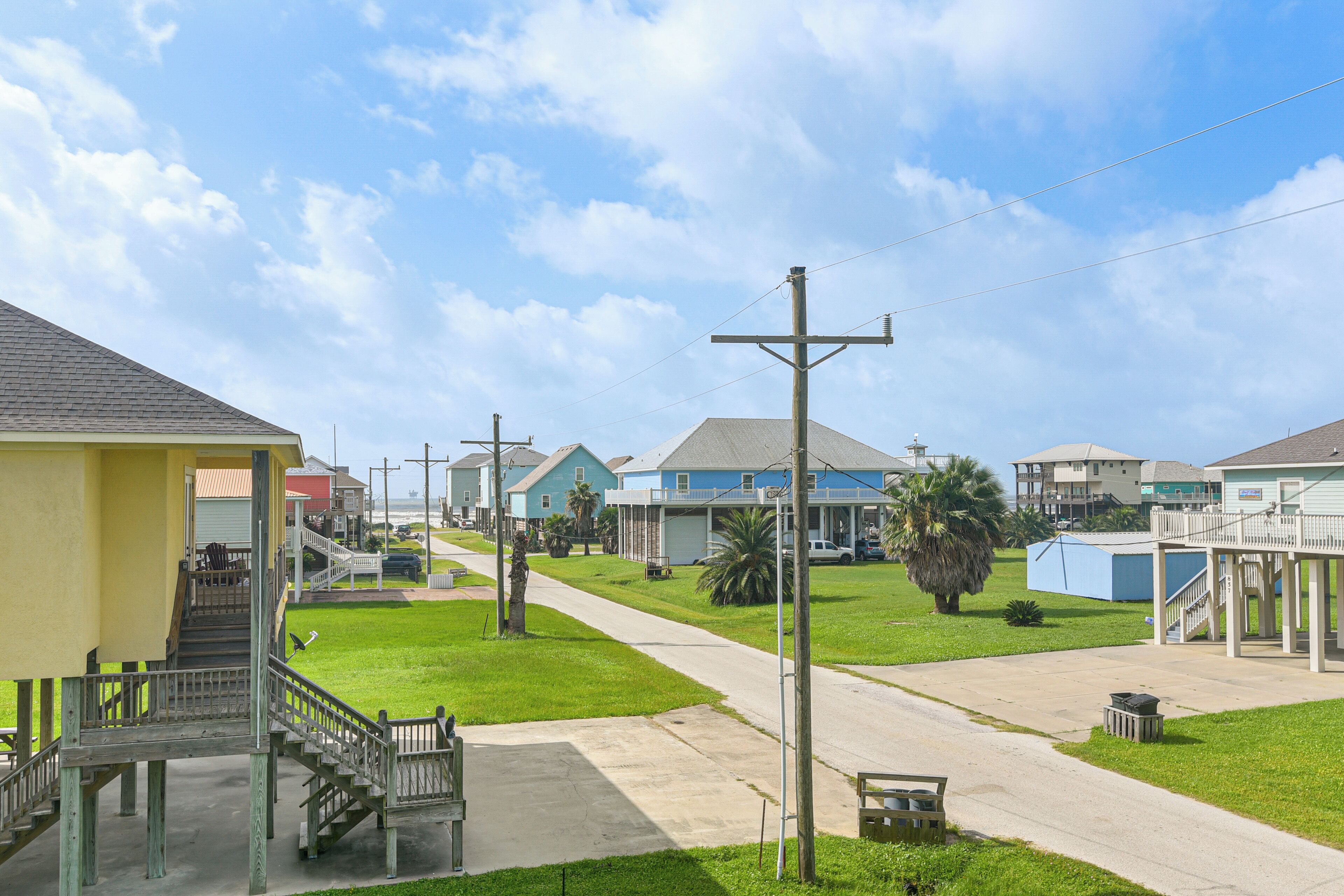 A residential street with houses, a sidewalk, and a grassy area.