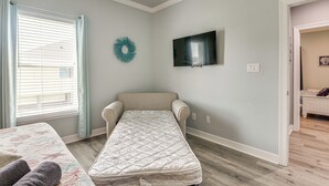 A room with a single bed, a television mounted on the wall, and a window with blinds. - Bolivar Peninsula Beach House: Family Friendly! (Port Bolivar)