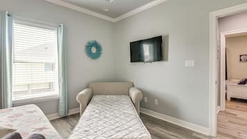 Quarto com uma cama de solteiro, televisão fixada na parede e janela com persianas.