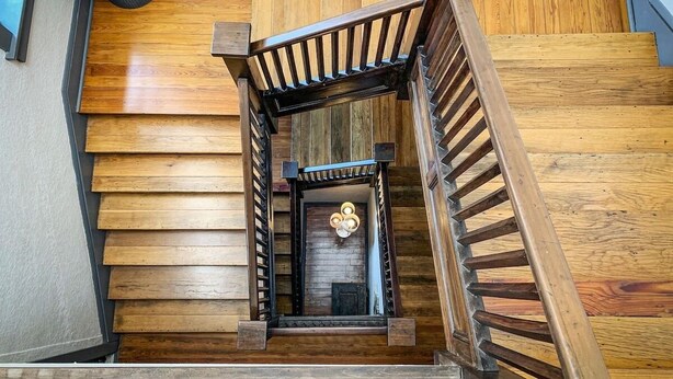 A wooden staircase with a metal railing, a potted plant, and a door with a light fixture.