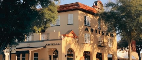 Un edificio de dos pisos con un letrero que dice 'ARTISAN' y una torre de campanas.