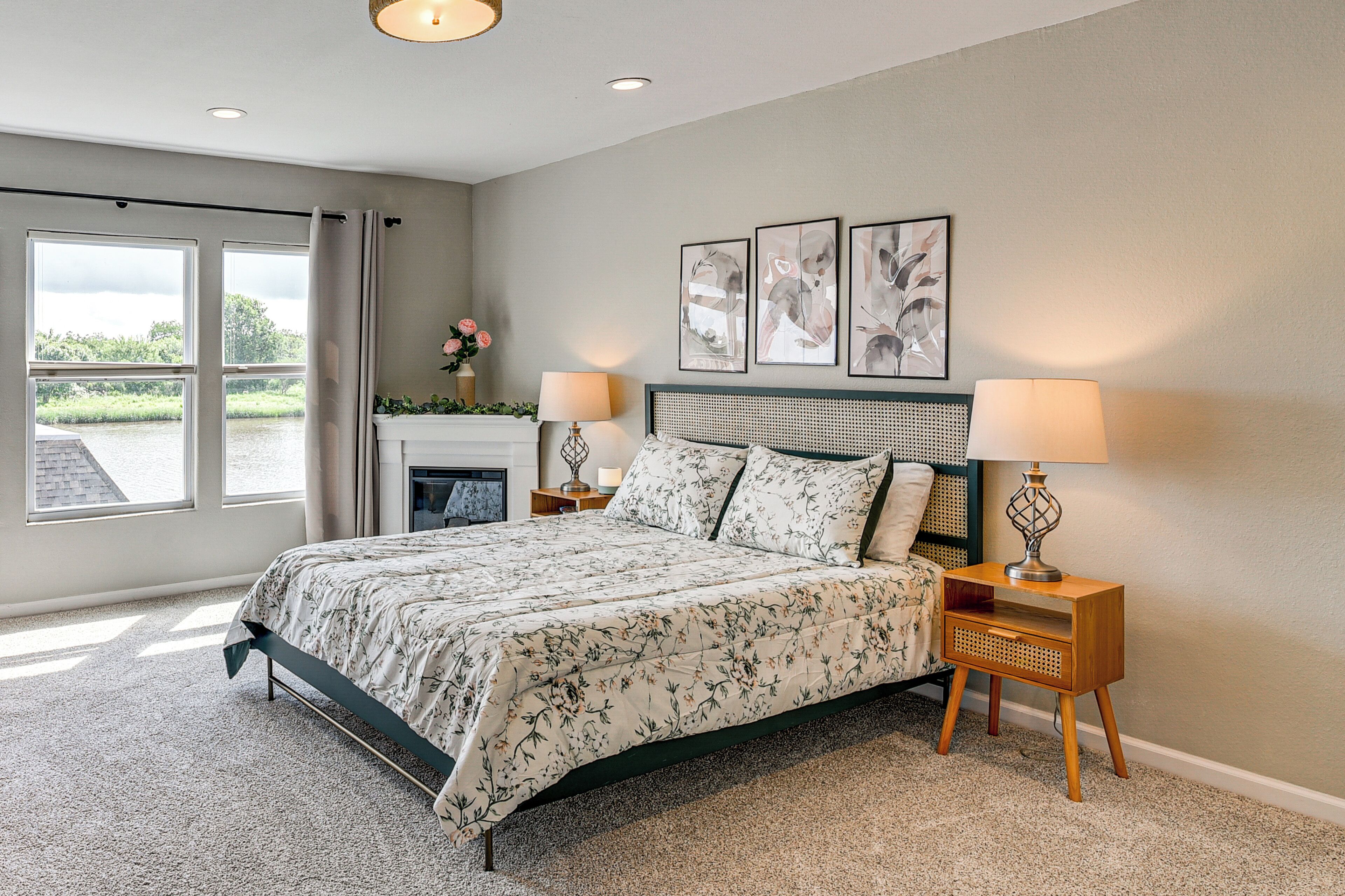 A bedroom with a bed, two bedside tables, a fireplace, and a view of greenery outside.