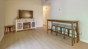 Ein Wohnzimmer mit einem Flachbildfernseher auf einer Kommode, einem Holztisch mit Barhocker und einem kleinen runden Tisch mit einem Stuhl.