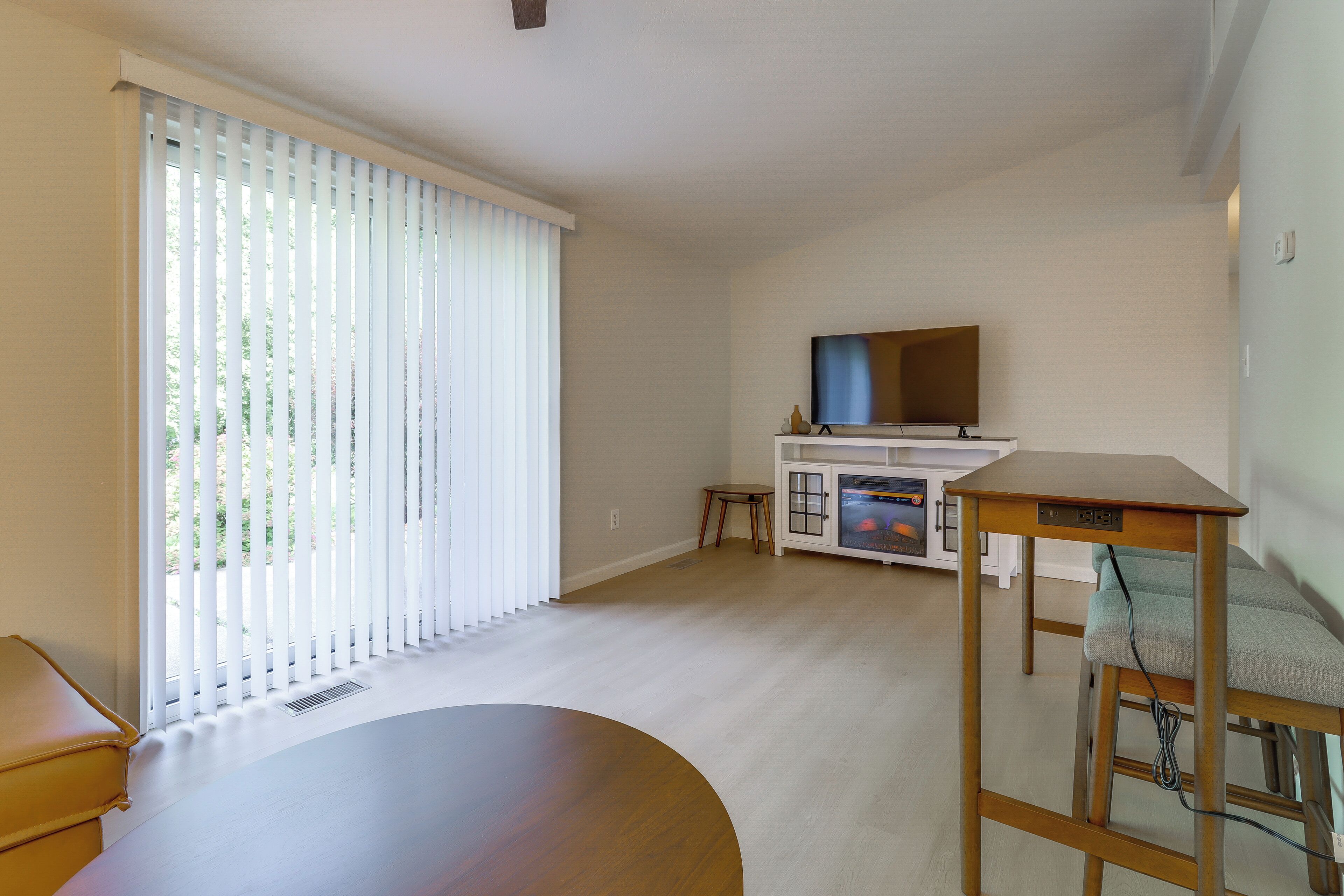 Ein Wohnzimmer mit großem Fenster, Flachbildfernseher, Holztisch und einer Couch.