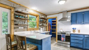 A kitchen with a central island, wooden chairs, a stove, and blue cabinets. - 7 Acres w/ Trails! Waynesville Adventure Hub (Waynesville)