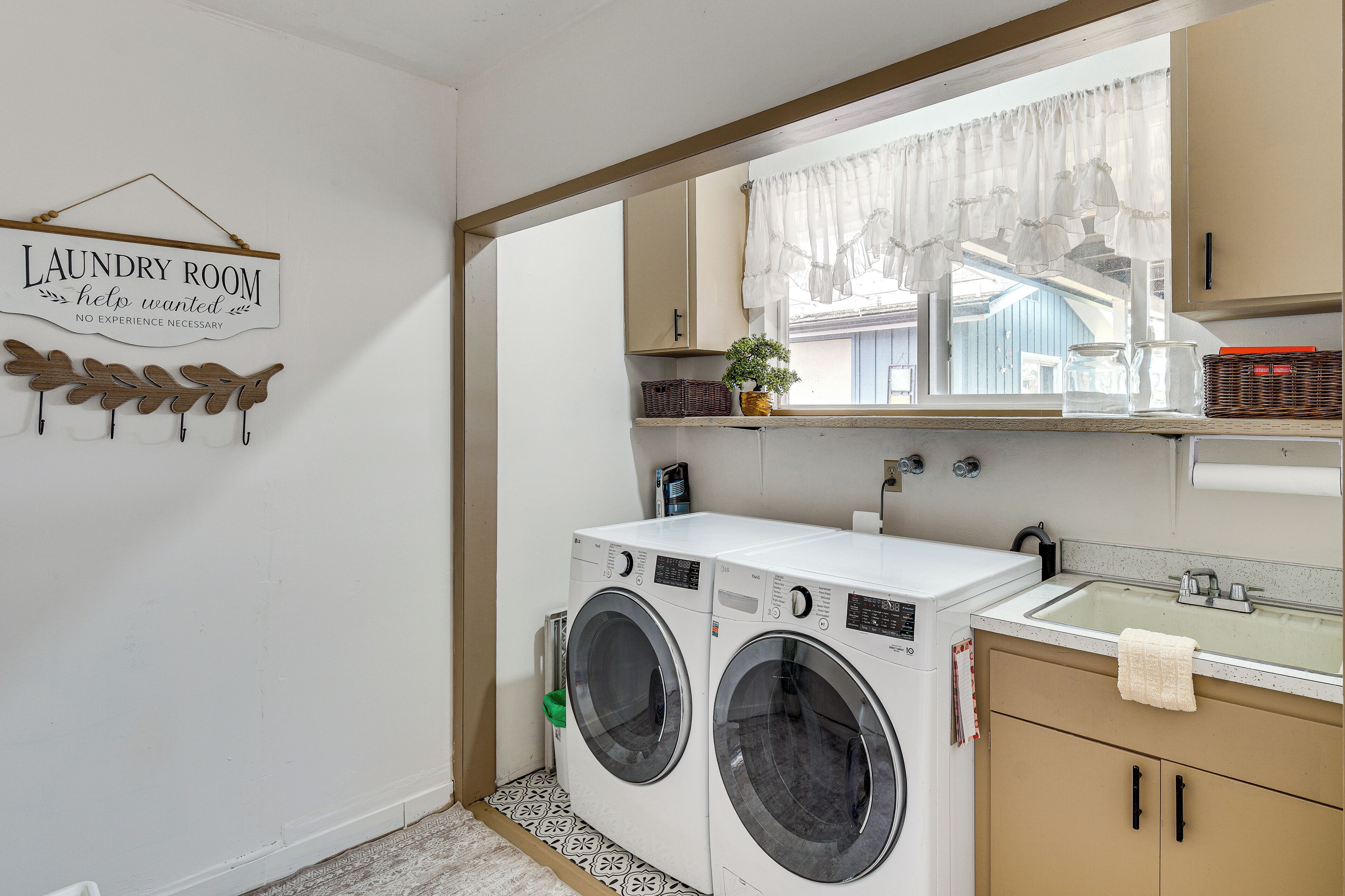 A laundry room with a sign, two washing machines, a sink, and a window with a view.