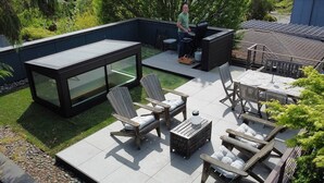 A patio with outdoor furniture, a grill, and a glass-enclosed area.