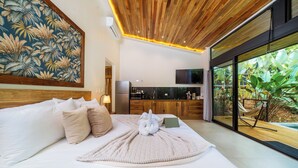 A modern bedroom with a large bed, a wooden ceiling, a kitchen area, and a view of greenery. - KARÉ: Arenal Exclusive Rainforest - Villa Senda (La Fortuna)