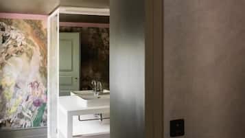 Un couloir orné d’une bordure à motifs, une salle de bain avec un lavabo et un miroir, et un sol aux couleurs vives.
