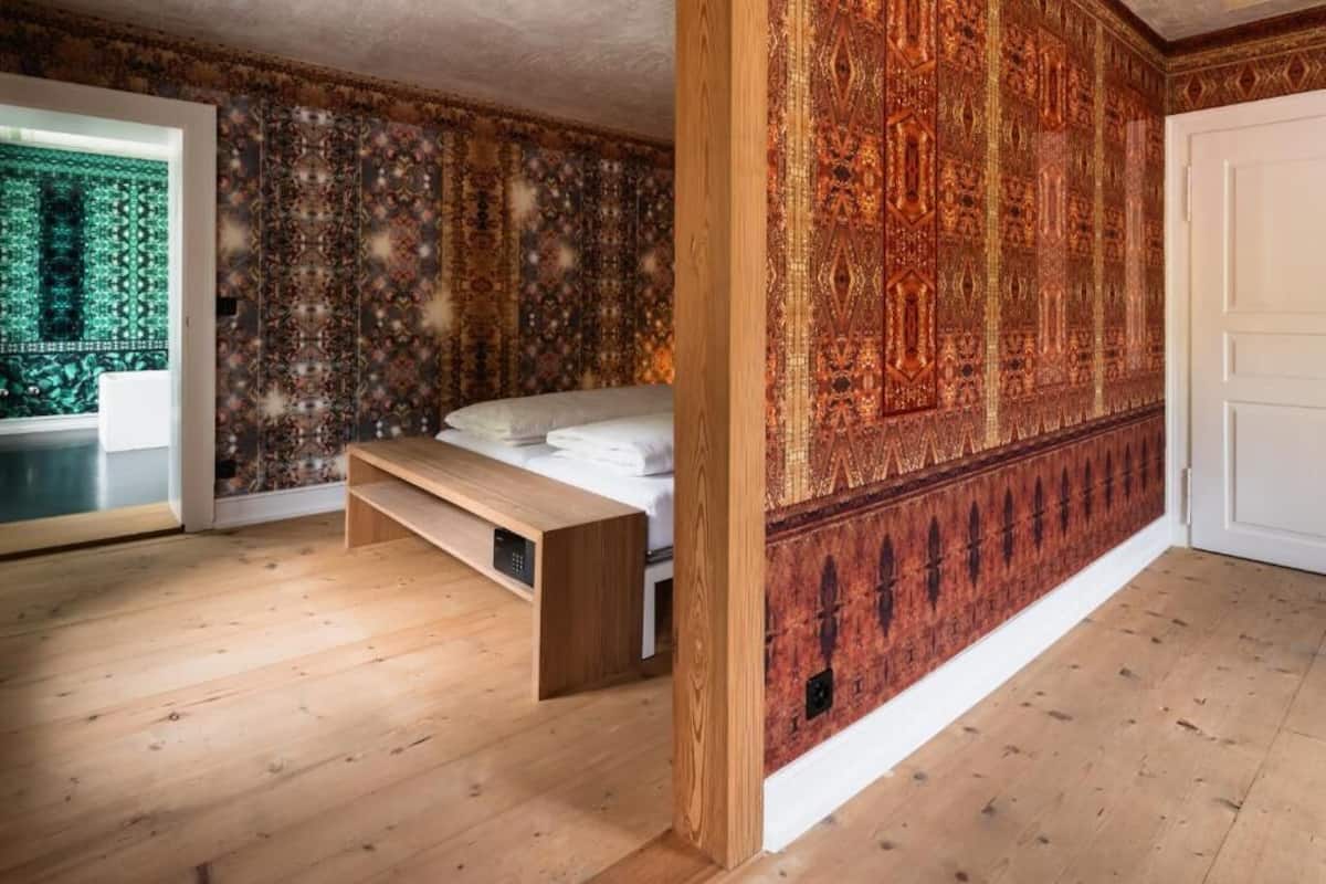 A bedroom with a bed, a bench, a patterned wall, and a door.