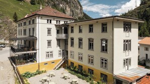A multi-story hotel with a balcony, outdoor seating area, and a mountain backdrop. - Post Hotel Löwe (Surses)