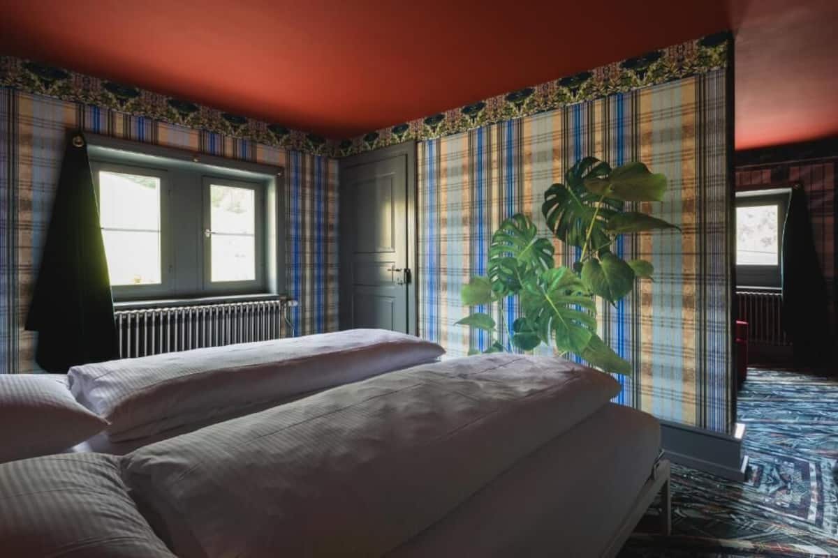 A room with a bed, a radiator, a window, and a large plant.