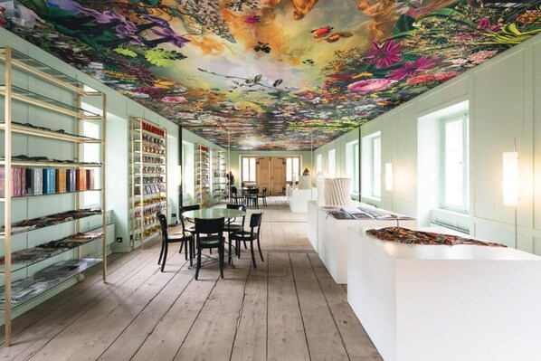A room with a wooden floor, bookshelves, a dining area, and a ceiling with a floral mural.