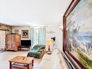 Ein Wohnzimmer mit Fernseher, einem Gemälde, einer Lampe und einer Holzkommode.