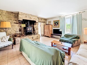Ein Wohnzimmer mit Steinwand, Kamin, Sofa, Fernseher und einem Fenster mit Vorhängen.