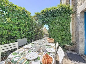 An outdoor dining area with a table set for two, surrounded by lush greenery and stone walls. - Keryargon by Interhome (Belz)