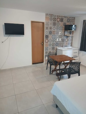 Quarto de hotel com cama, escrivaninha com cadeira, televisão e painel de azulejos.