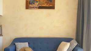 A blue sofa with patterned cushions, a small round table with a glass of orange juice, and a framed artwork above. - Appartement de charme vue sur mer (Valle-di-Campoloro)