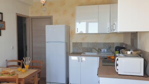 A compact kitchen with a refrigerator, a sink, and a dining area with chairs and a table. - Appartement de charme vue sur mer (Valle-di-Campoloro)
