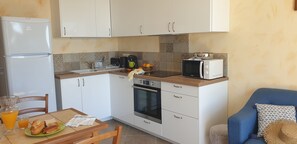 A compact kitchen with white cabinets, a microwave, a coffee maker, and a dining area with a table and chairs. - Appartement de charme vue sur mer (Valle-di-Campoloro)
