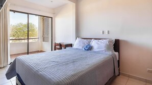 Une chambre d’hôtel avec un lit, une petite table, une chaise, un balcon avec vue et un ventilateur de plafond.
