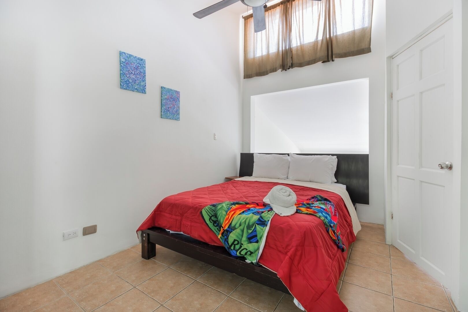 Un dormitorio con cama, ventilador de techo, ventana con cortinas y puerta.