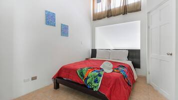 Un dormitorio con cama, ventilador de techo, ventana con cortinas y puerta.