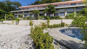 A hotel with a swimming pool, surrounded by a pebble beach and greenery.