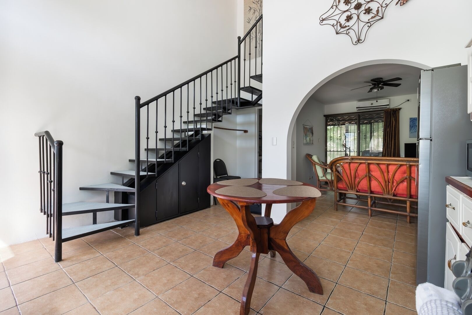 A staircase with black railings, a dining area with a round table, and a kitchen area with a refrigerator.