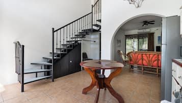 A staircase with black railings, a dining area with a round table, and a kitchen area with a refrigerator.