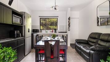 A modern kitchen with a dining area, a black leather sofa, and a ceiling fan.